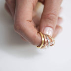 A hand holding four gold Coordinates Bands with engraved text, displayed against a plain white background—each ring represents a special memory to treasure.