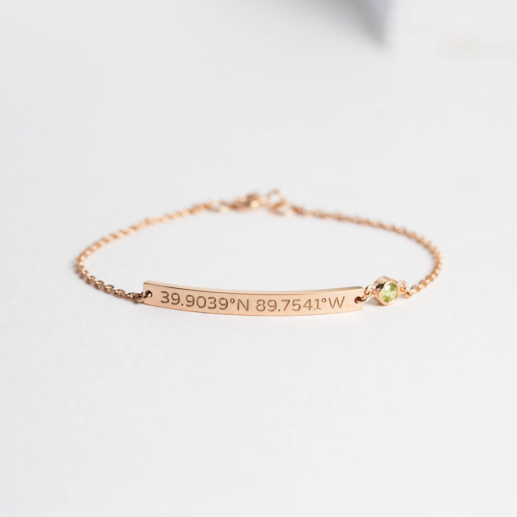 The Thin Coordinates Bar Bracelet in rose gold features custom location engraving and a small yellow gemstone, shown on a white background.
