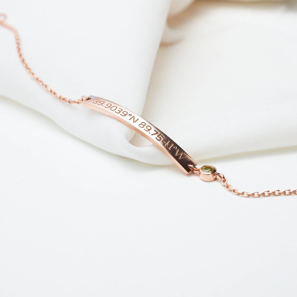 The Thin Coordinates Bar Bracelet in rose gold features a slim bar engraved with your custom location, creating elegant, personalized jewelry. Displayed on a white fabric background for a refined touch.