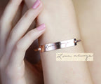 A hand with pink nails wears a Handwriting Bar Bangle engraved with "Love always" in cursive.