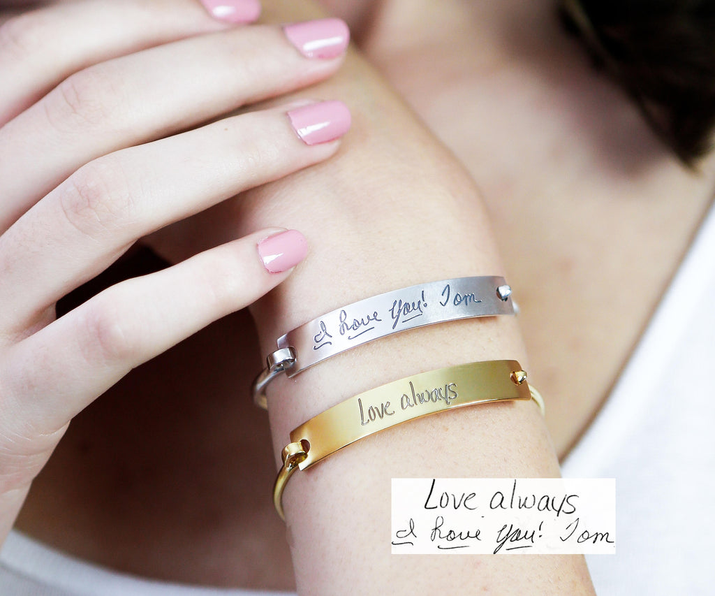 A woman wears two Handwriting Bar Bangles—one engraved with "Love always," the other with "I love you! Tom." These custom bangles are unique personalized keepsakes that capture heartfelt messages in your own handwriting.
