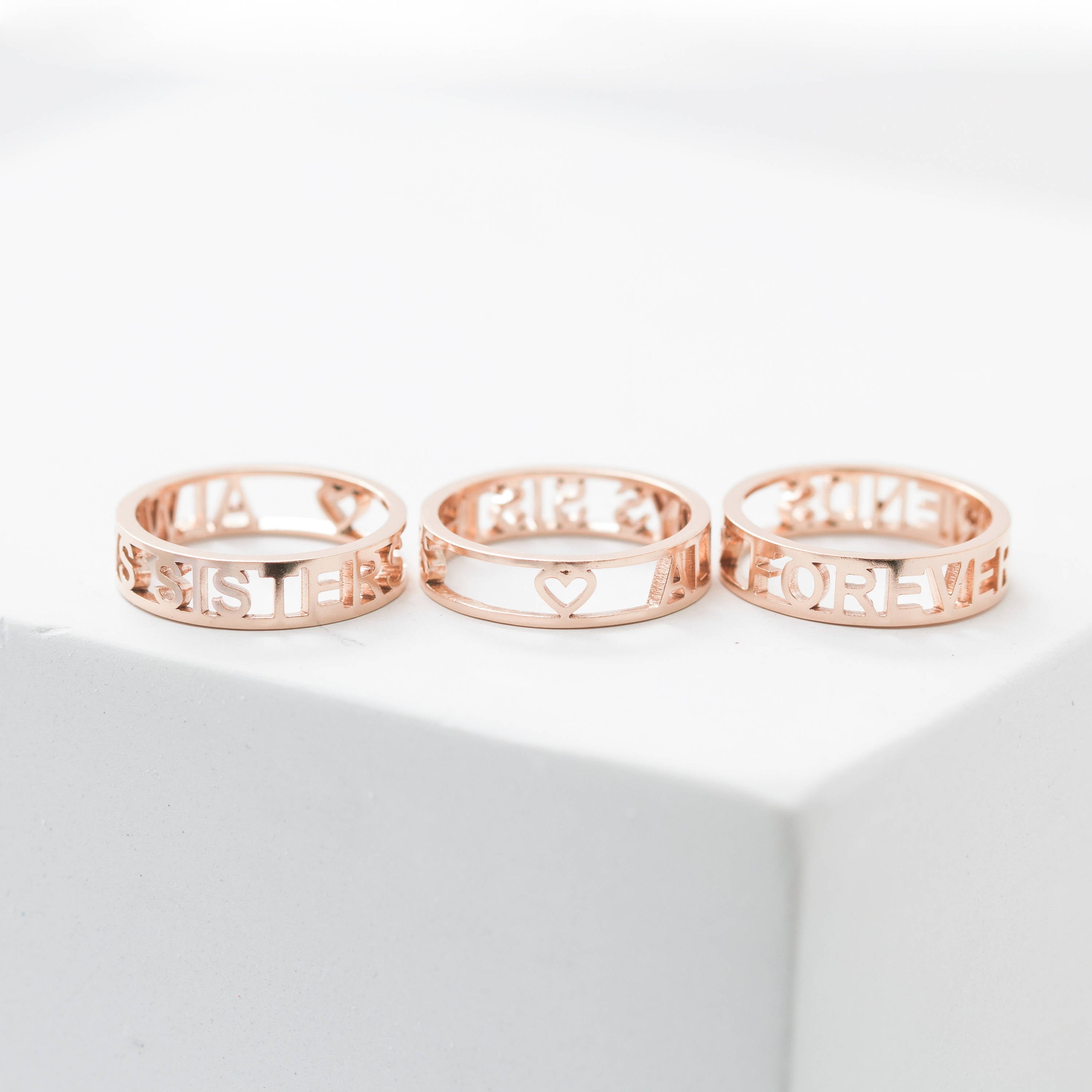 The Roman Numerals Ring in Rose Gold—featuring elegant cutout numbers and a heart design—is displayed on a white surface, making it a perfect choice for commemorating a personal milestone.