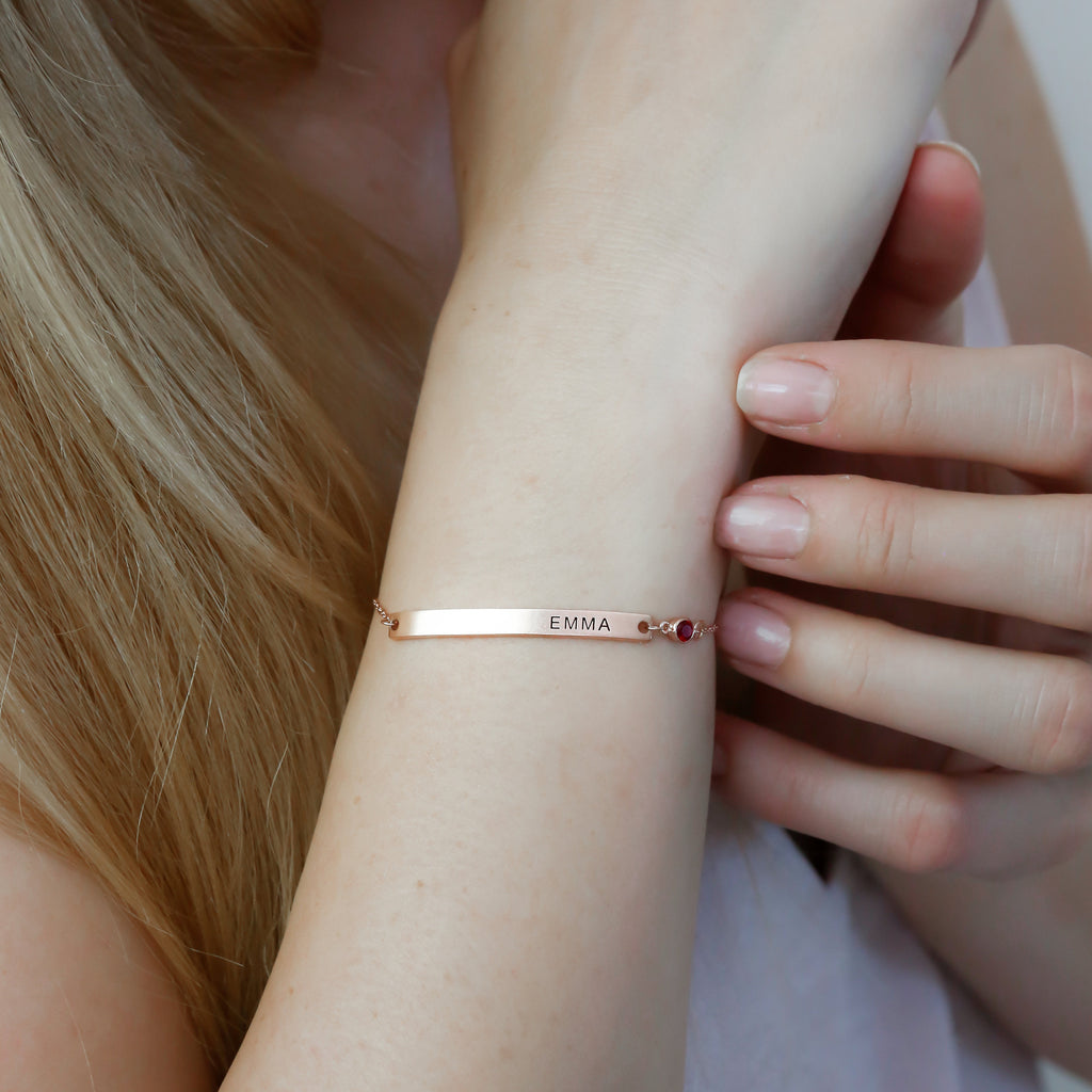 A woman wears a Thin Name Bar Bracelet engraved with EMMA on her wrist, showcasing elegant personalized jewelry.