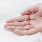 A hand holds two small London Name Earrings shaped like the word “Charlotte” in elegant script font.
