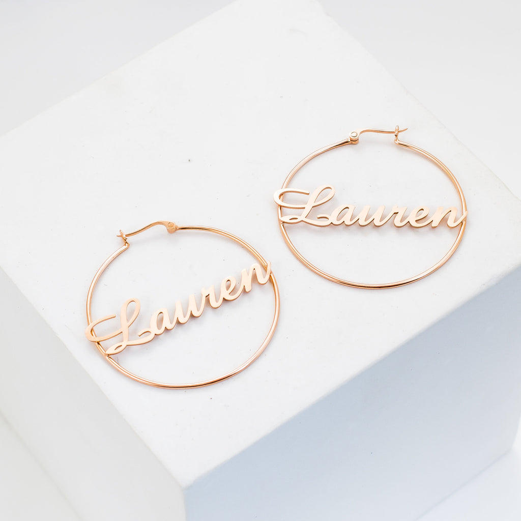 Classic Name Hoops featuring "Lauren" in cursive gold, displayed on a white cube. Perfect personalized jewelry for fans of stylish name earrings.