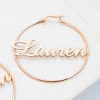 Classic Name Hoops feature gold hoop earrings with the name Lauren in cursive across the center—ideal for personalized jewelry lovers and stylish accessory fans, shown on a white surface.