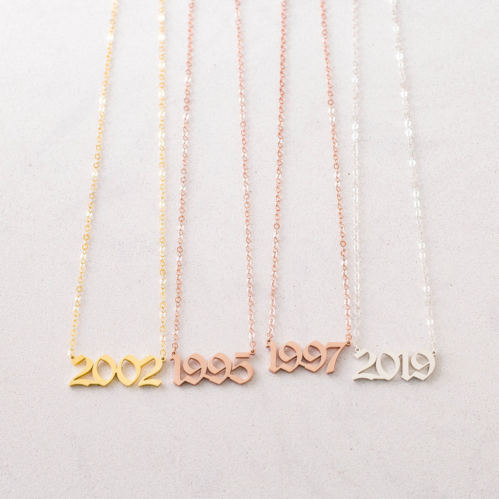The Year Necklace comes in gold, rose gold, and silver with number pendants—2002, 1995, 1997, and 2019. Each necklace offers a personalized touch to your style.