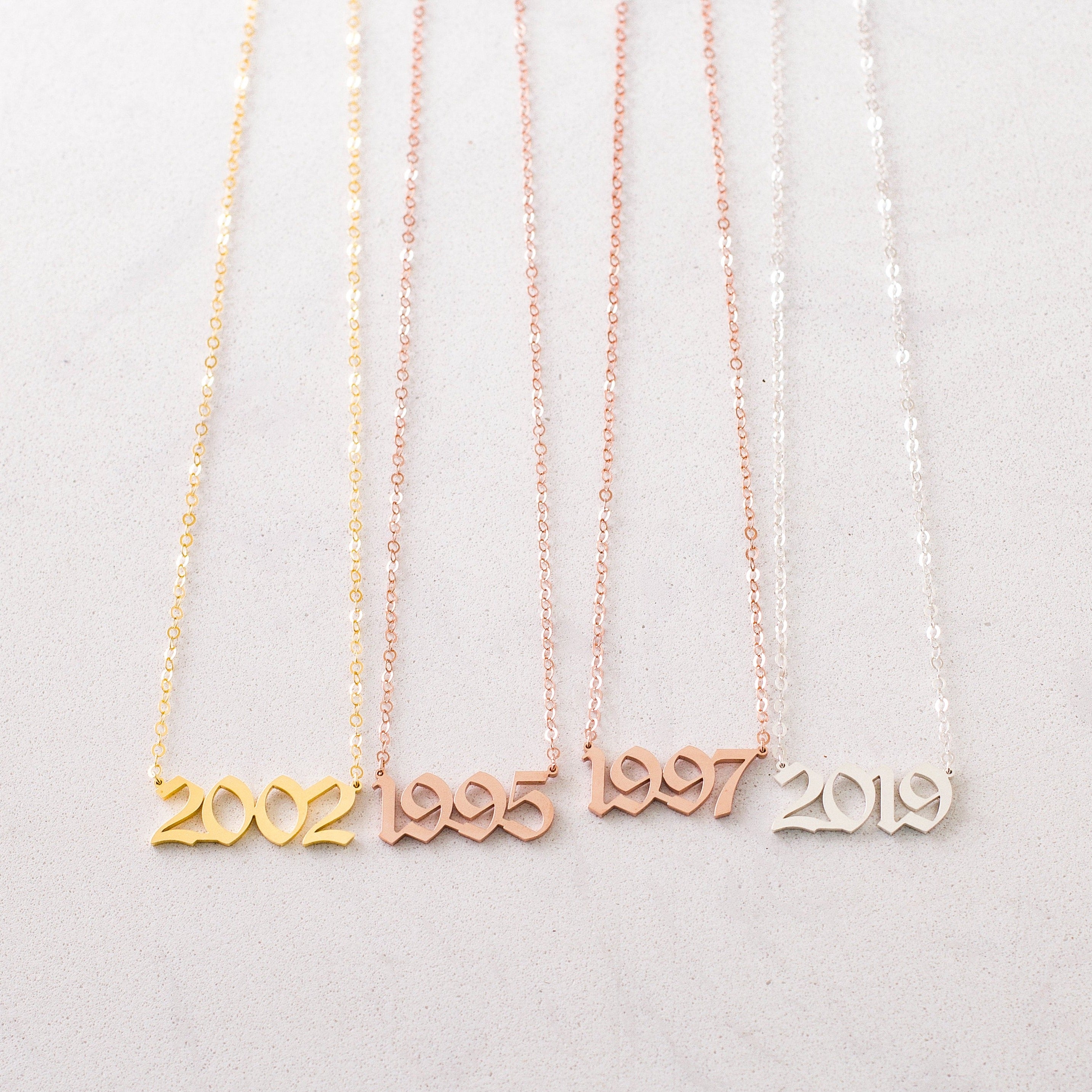 The Year Necklace comes in gold, rose gold, and silver with number pendants—2002, 1995, 1997, and 2019. Each necklace offers a personalized touch to your style.