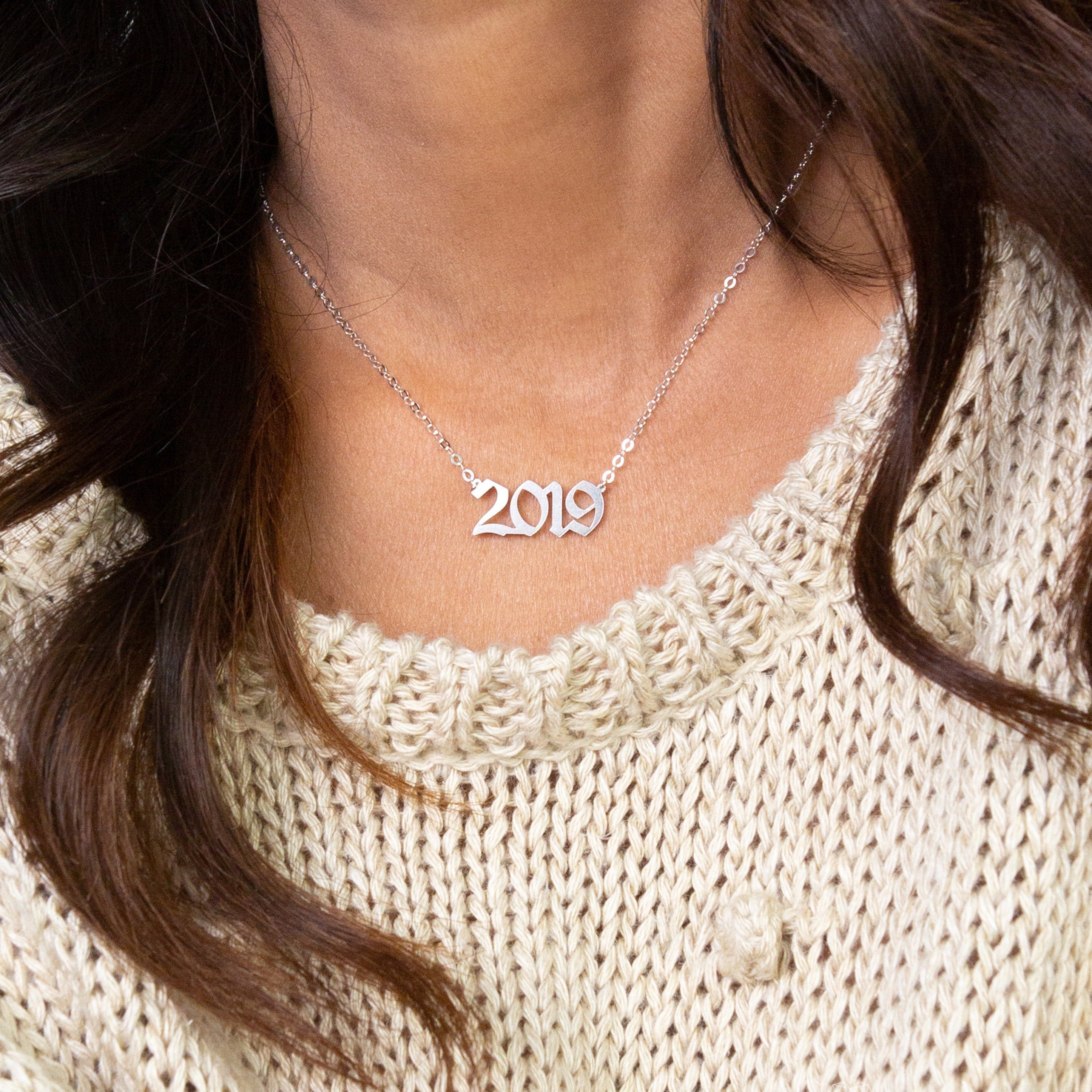 A woman wearing a silver Year Necklace for 2019 and a cream-colored knit sweater.