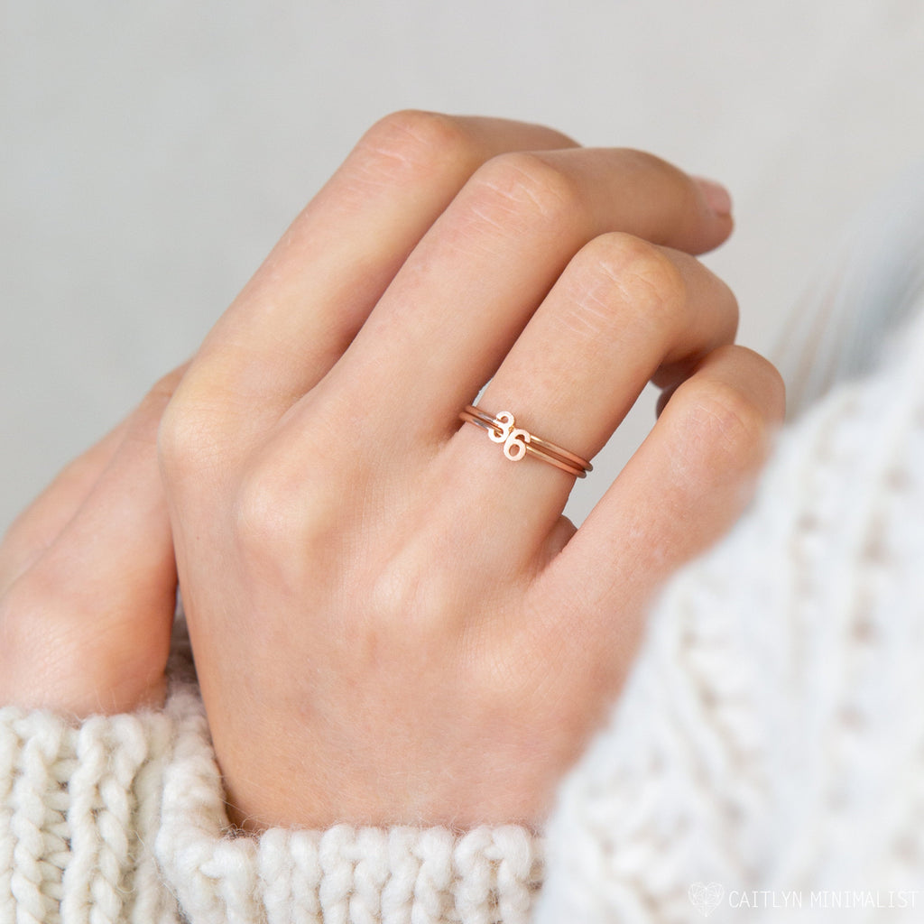 A hand wears the Alex Dainty Letter Ring in Rose Gold, featuring a minimalist Cancer zodiac sign—ideal for lovers of personalized, delicate jewelry.