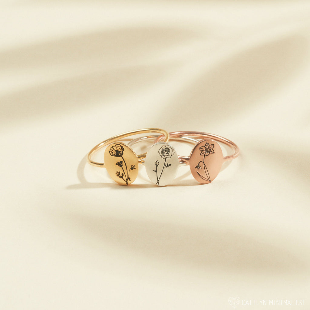 Three gold Birth Flower Oval Rings with engraved floral designs, ideal for personalized jewelry, showcased on a cream background.