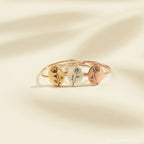 Three gold Birth Flower Oval Rings with engraved floral designs, ideal for personalized jewelry, showcased on a cream background.