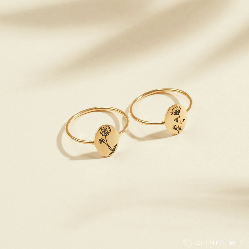 Two gold Birth Flower Oval Rings with engraved floral designs on oval faces are displayed on a light beige background—ideal personalized jewelry to honor your birth month flower.