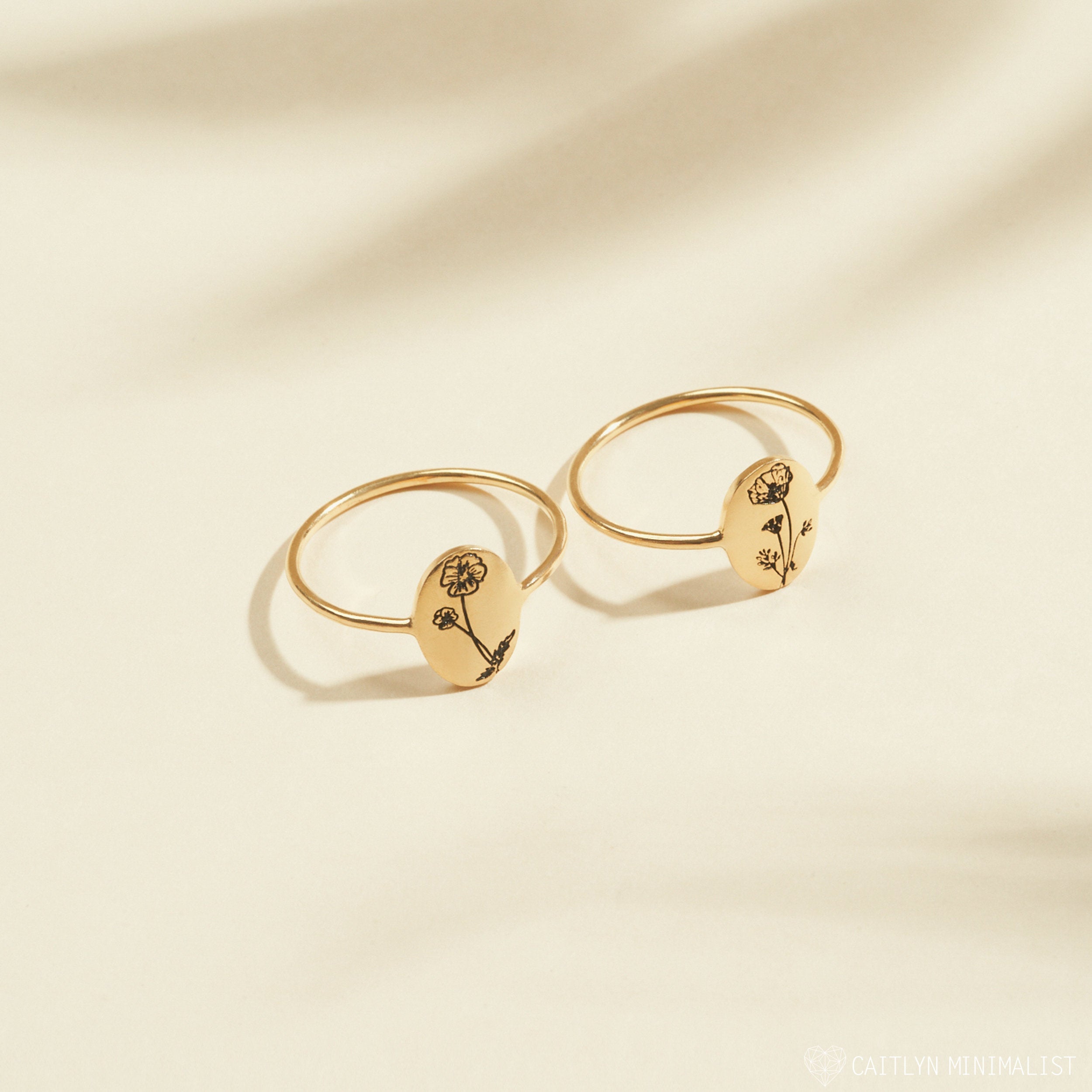 Two gold Birth Flower Oval Rings with engraved floral designs on oval faces are displayed on a light beige background—ideal personalized jewelry to honor your birth month flower.