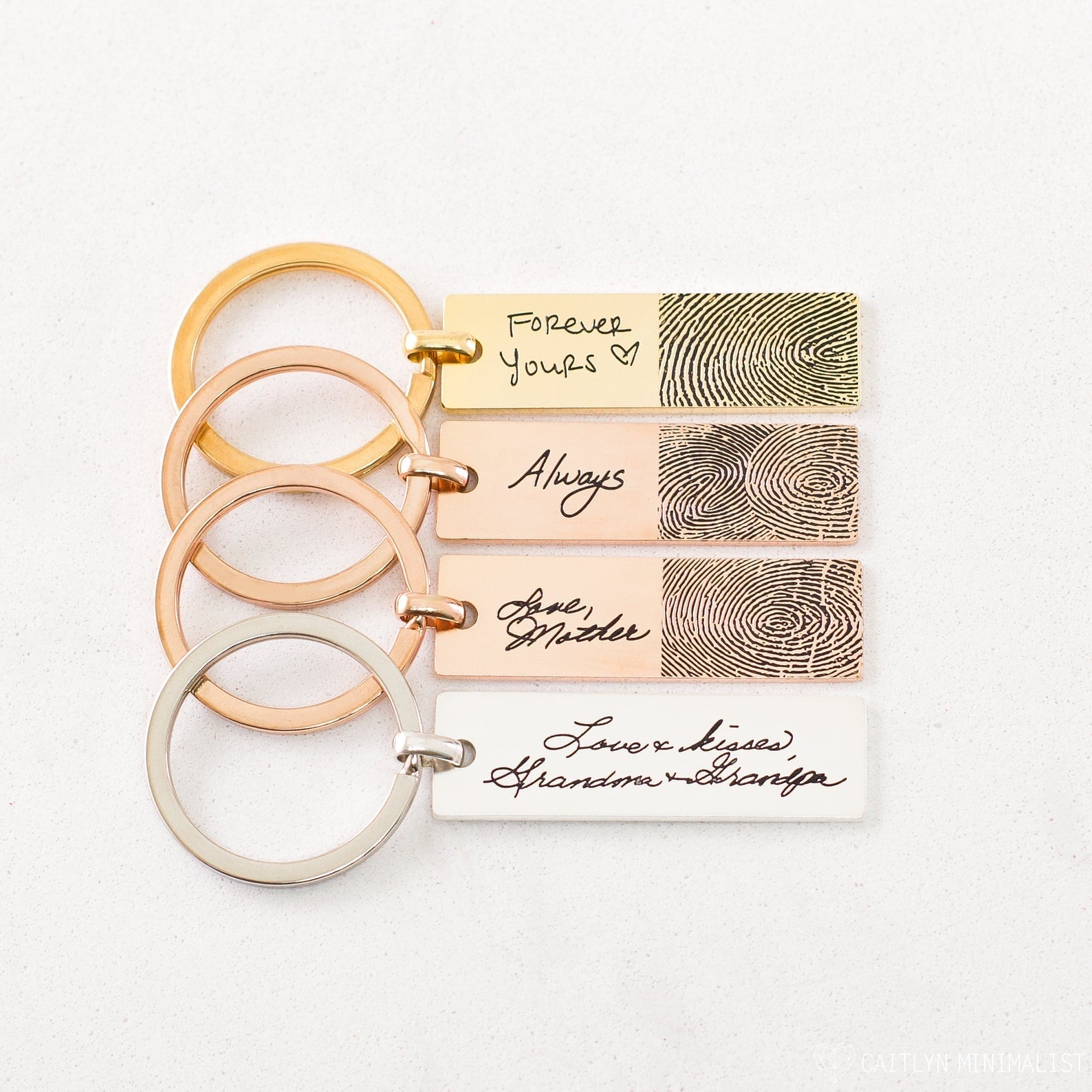 Four Fingerprint Bar Keychains—each engraved with a fingerprint and message in different metallic colors—create a unique personalized keepsake, shown here on a white surface.