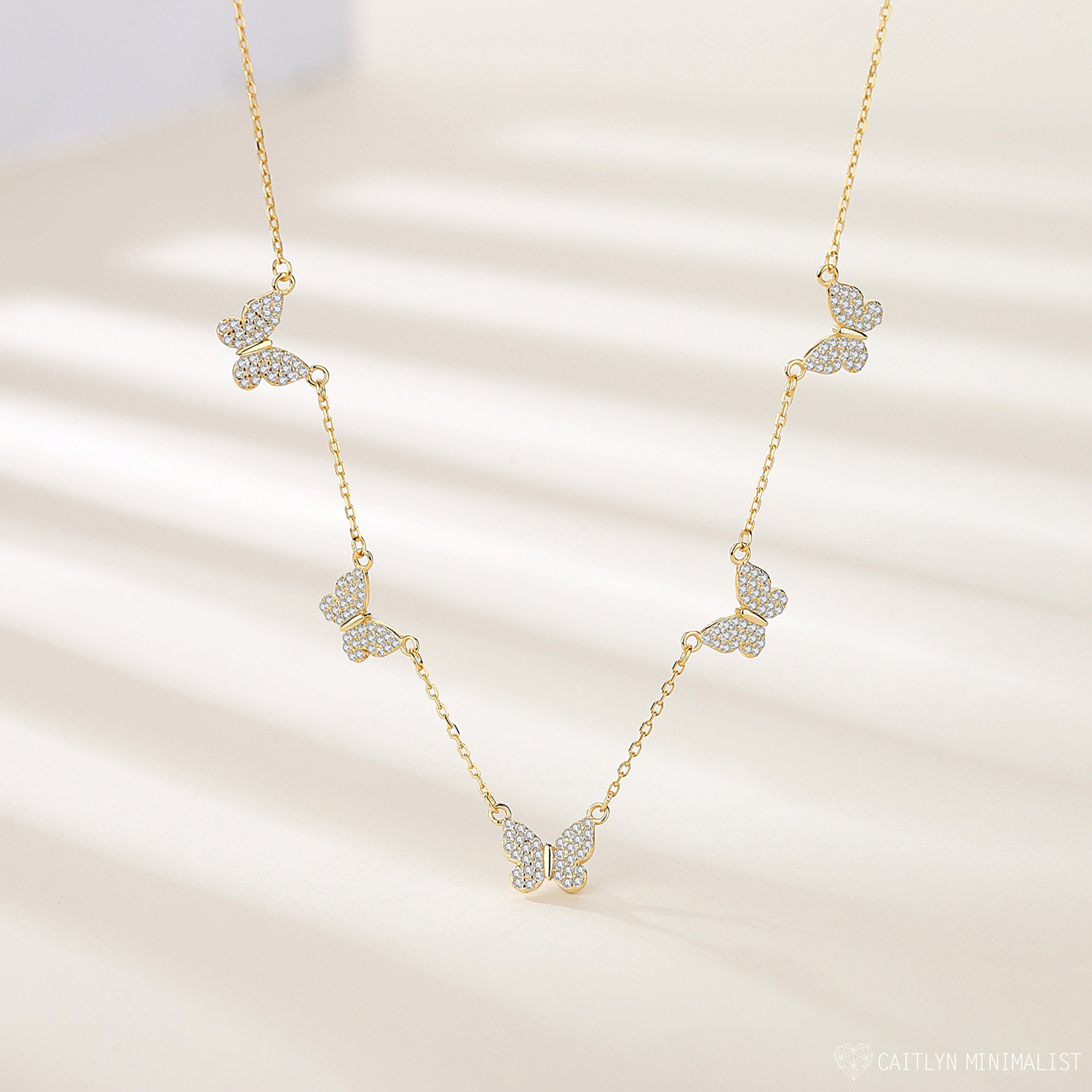 The Pave Butterfly Necklace features five diamond-encrusted butterfly pendants adorned with sparkling stones, elegantly displayed on a light background.