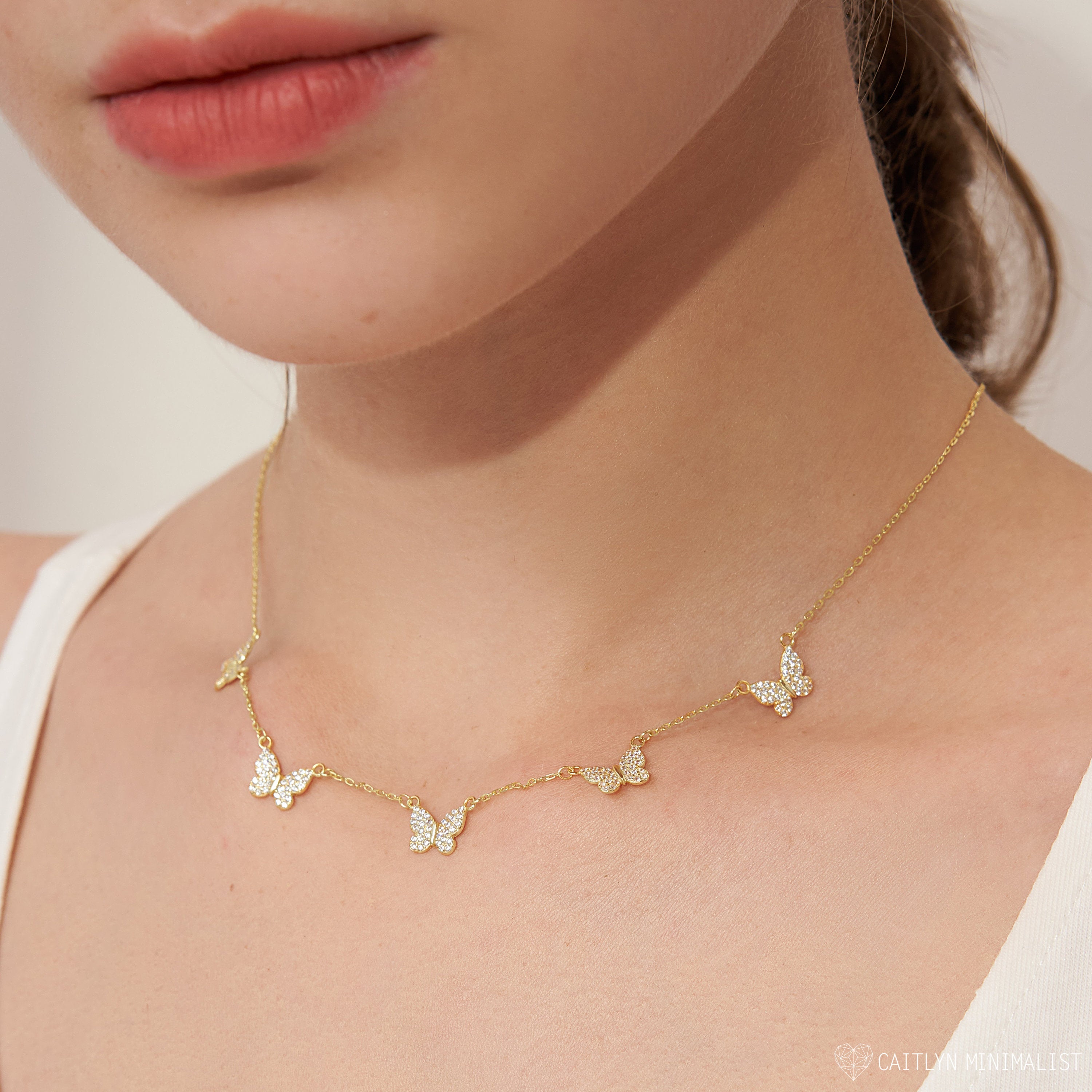 A woman wears the Pave Butterfly Necklace, featuring five small, diamond-encrusted butterflies that sparkle delicately along this feminine piece.
