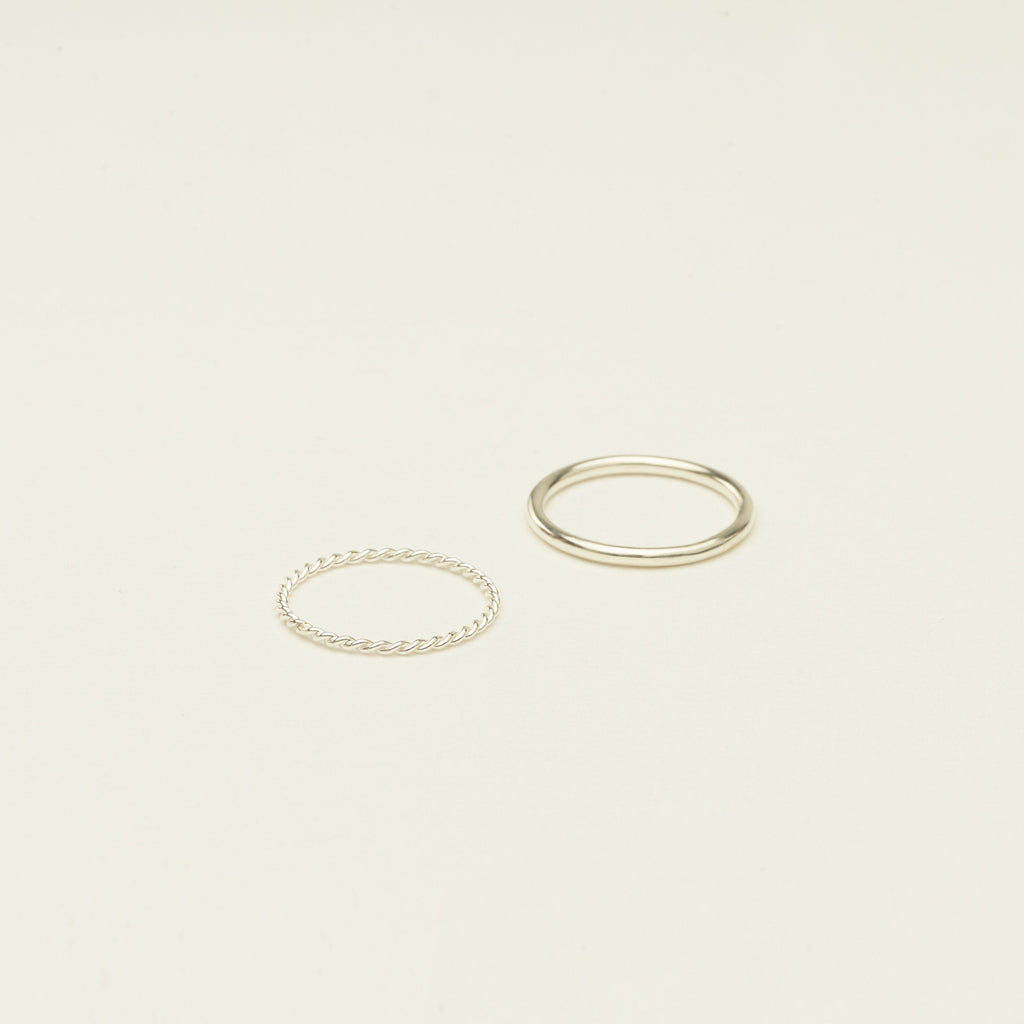 The Minimalist Stacking Ring Set features two silver rings—one twisted, one smooth—creating an elegant, minimalist look on a plain light background.