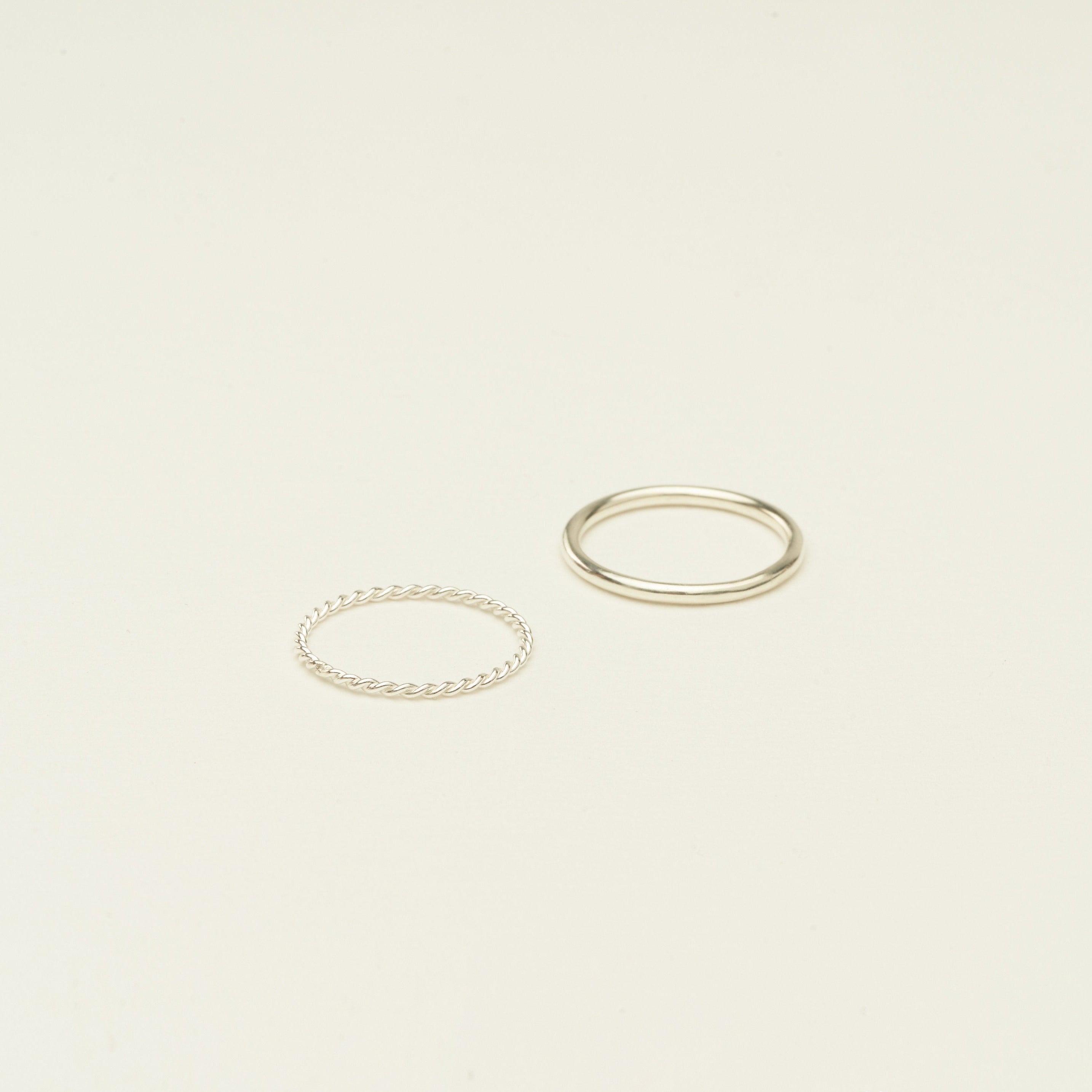 The Minimalist Stacking Ring Set features two silver rings—one twisted, one smooth—creating an elegant, minimalist look on a plain light background.