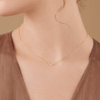 A woman wears the Lucia Pave Necklace, featuring a delicate crescent charm pendant, paired with a brown V-neck top.