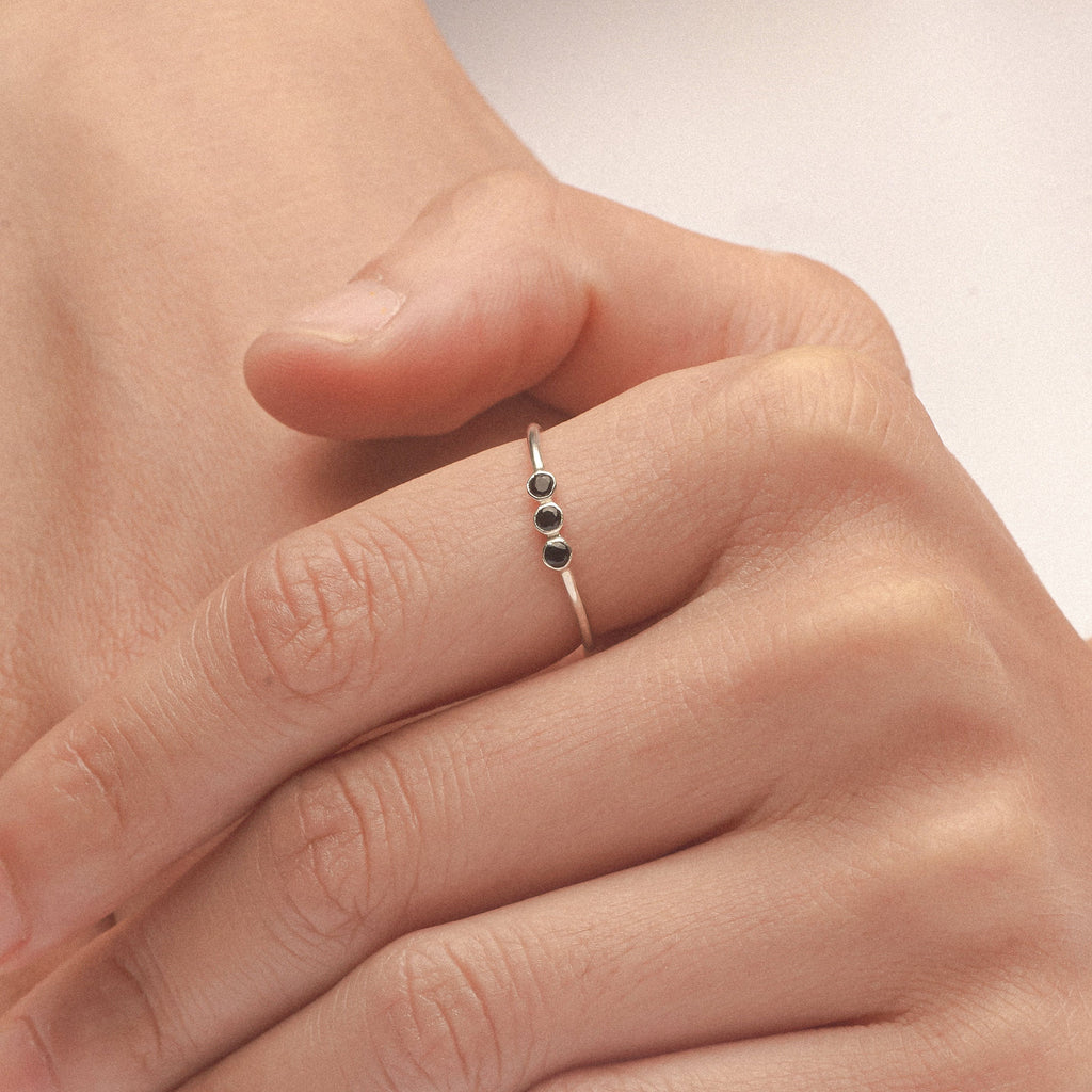 A hand wearing the Tiny Triple Birthstone Ring, showcasing a thin band and delicate sparkle from three dainty birthstones.