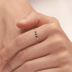 A hand wearing the Tiny Triple Birthstone Ring, showcasing a thin band and delicate sparkle from three dainty birthstones.