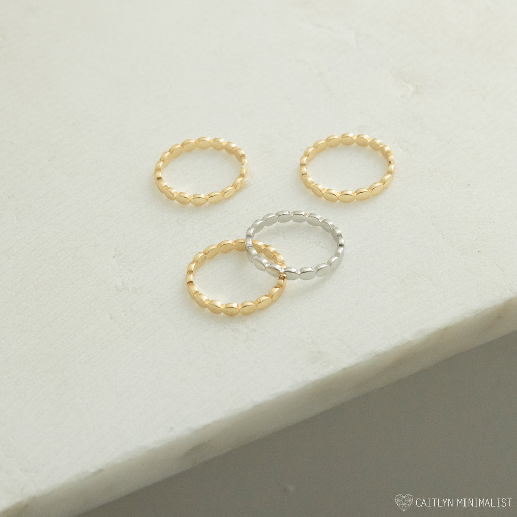 Four Beaded Rings—three gold and one silver—rest on a light textured surface, perfect for stacking as chic stackable bands or mixing into your textured jewelry collection.