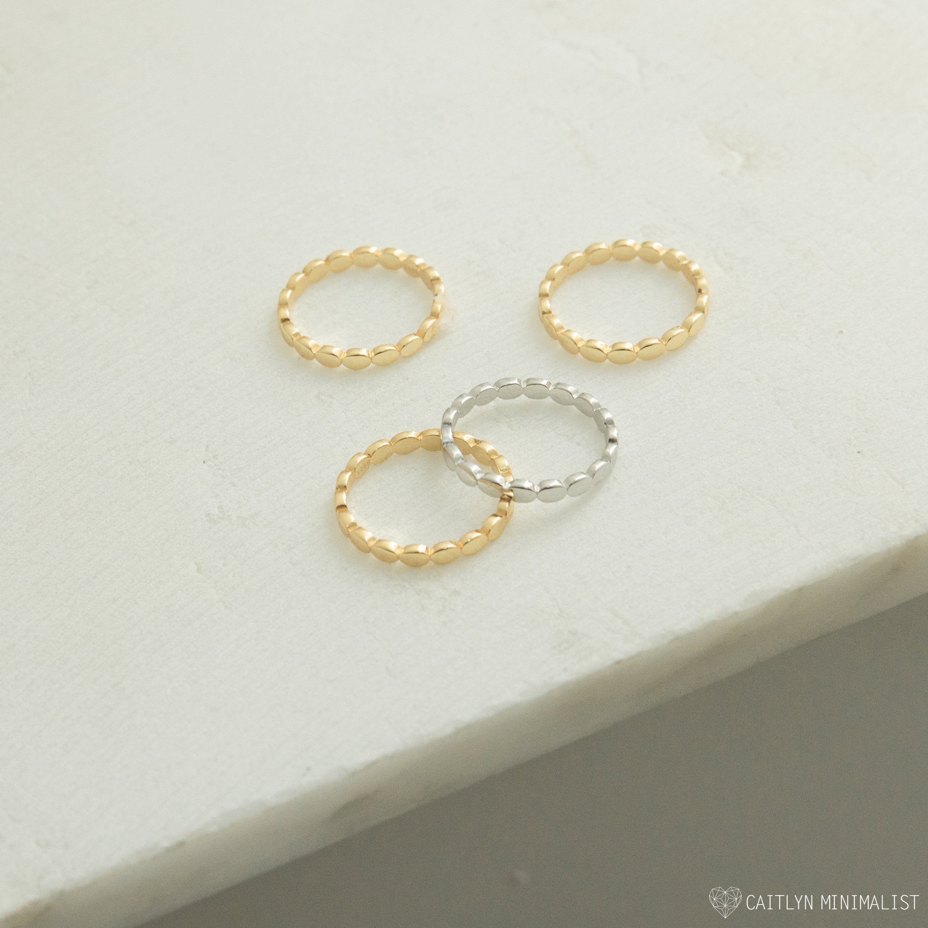Four Beaded Rings—three gold and one silver—rest on a light textured surface, perfect for stacking as chic stackable bands or mixing into your textured jewelry collection.