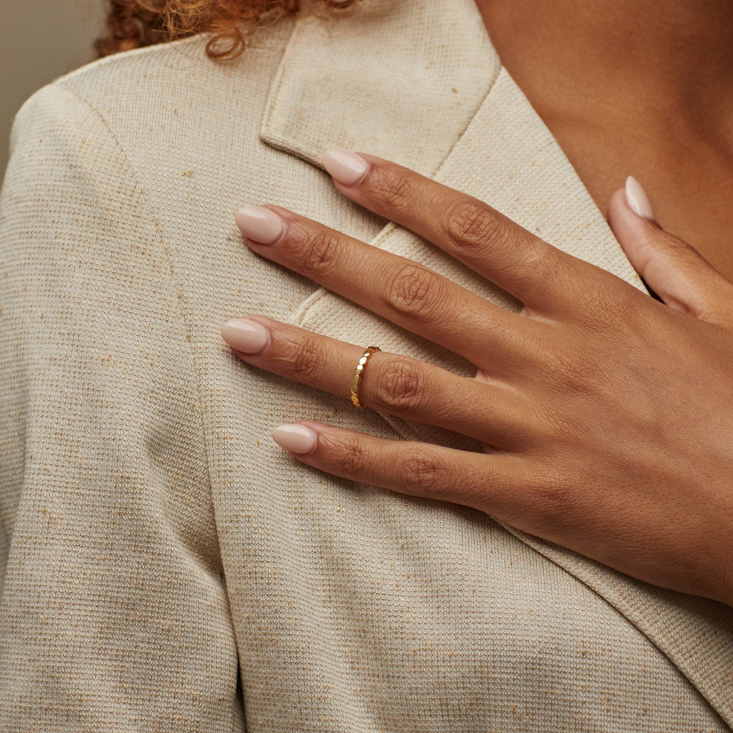 A hand with manicured nails wearing the Beaded Ring rests on a beige textured blazer.