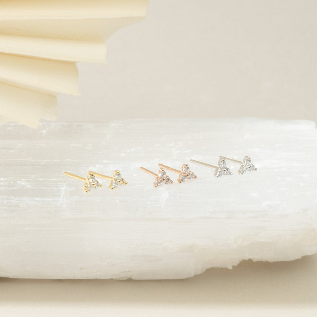 The Mini Lily Studs in Sterling Silver—small, triangle-shaped earrings perfect for cartilage piercings—are displayed on a white textured surface.