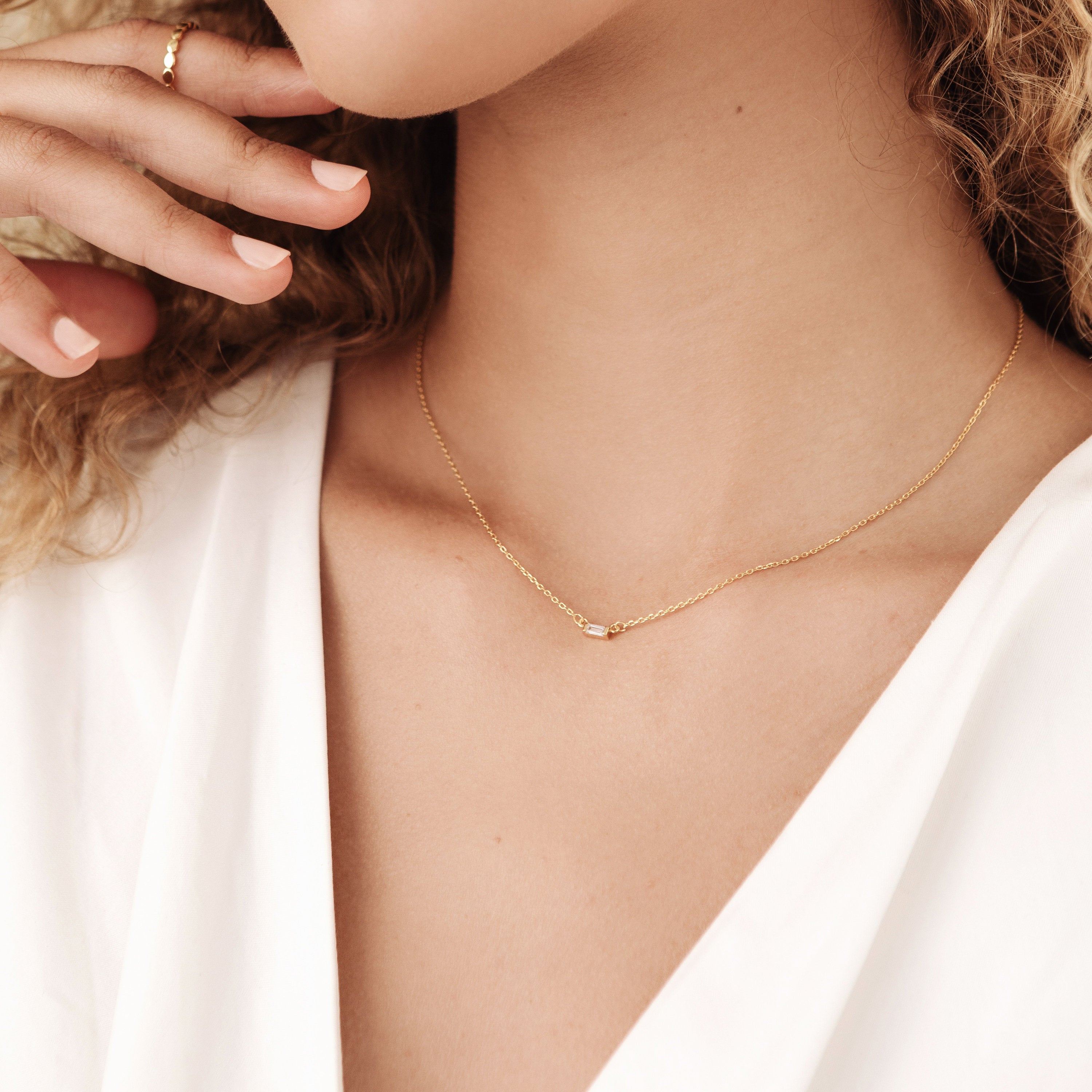 A woman in a white blouse wears a delicate sterling silver minimal necklace and a ring—the perfect look for holiday gifting, like the Emery Necklace in Sterling Silver.