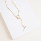 The Skyy Toggle Necklace features a gold bar pendant, ideal for minimal jewelry lovers. Shown on a textured white rectangular surface.