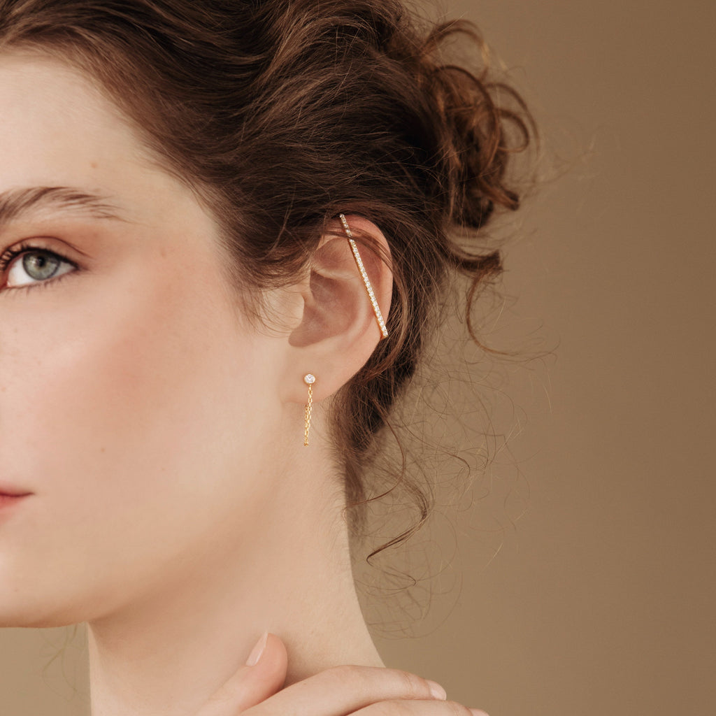 Woman with curly hair facing sideways on a neutral background, wearing Bar Ear Cuffs and delicate pave bar earrings.