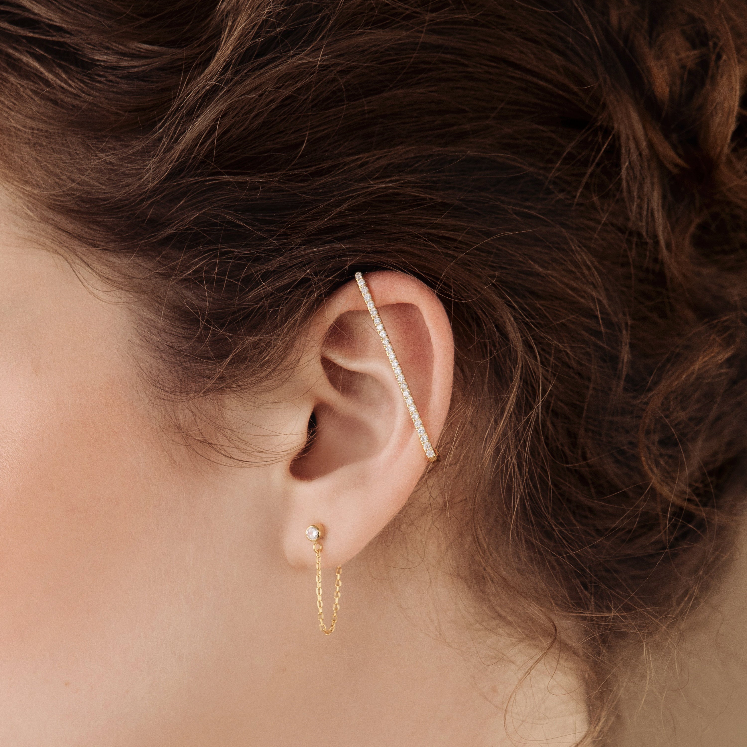 Close-up of an ear wearing gold hoops, a stud, and Bar Ear Cuffs adorned with small pavé gems.