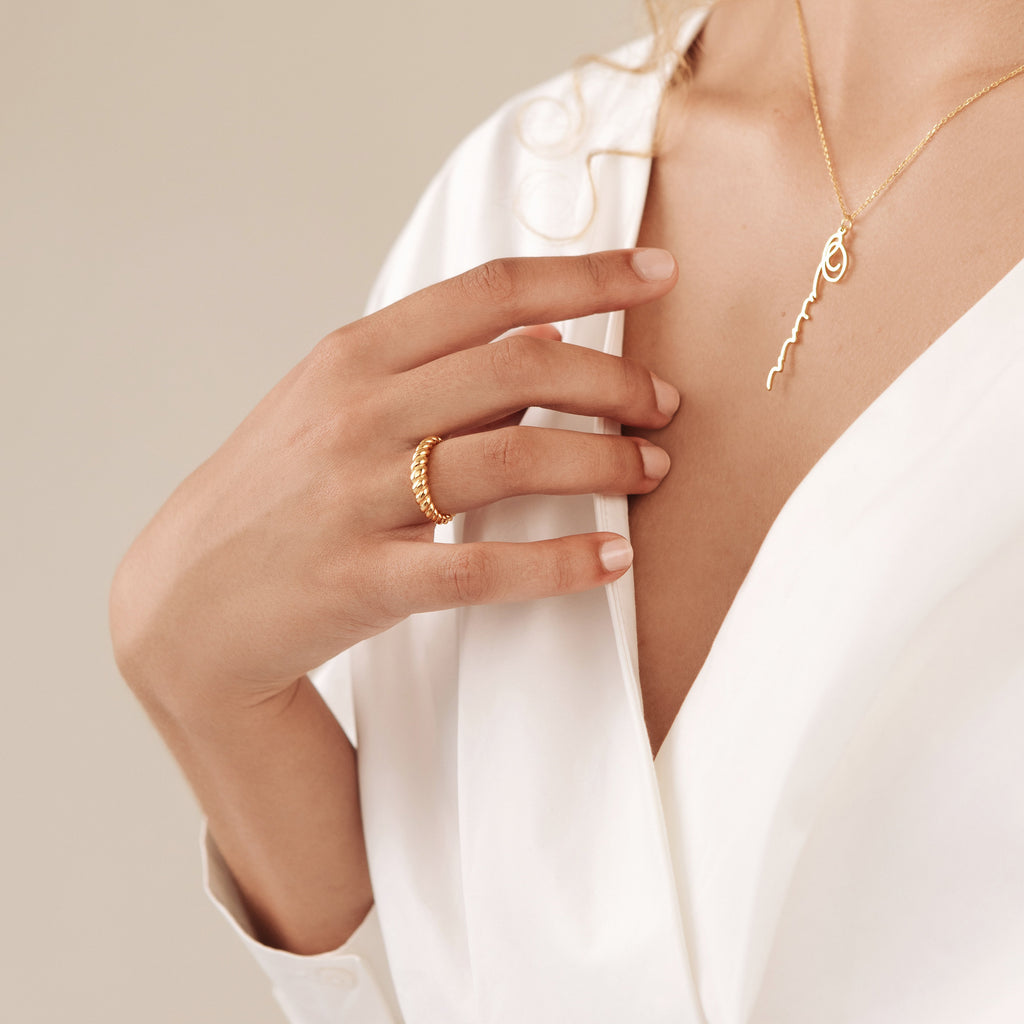Woman in a white blouse wearing the Twisted Dome Ring and a gold necklace with a delicate script pendant.