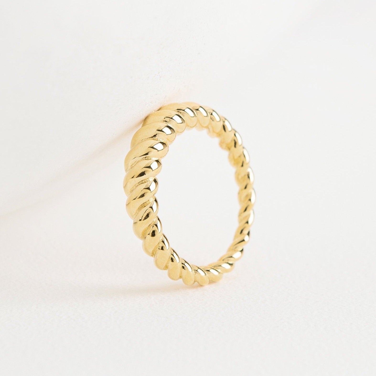 The Twisted Dome Ring stands upright on a white surface, its elegant gold curves highlighted against a minimal, clean background.