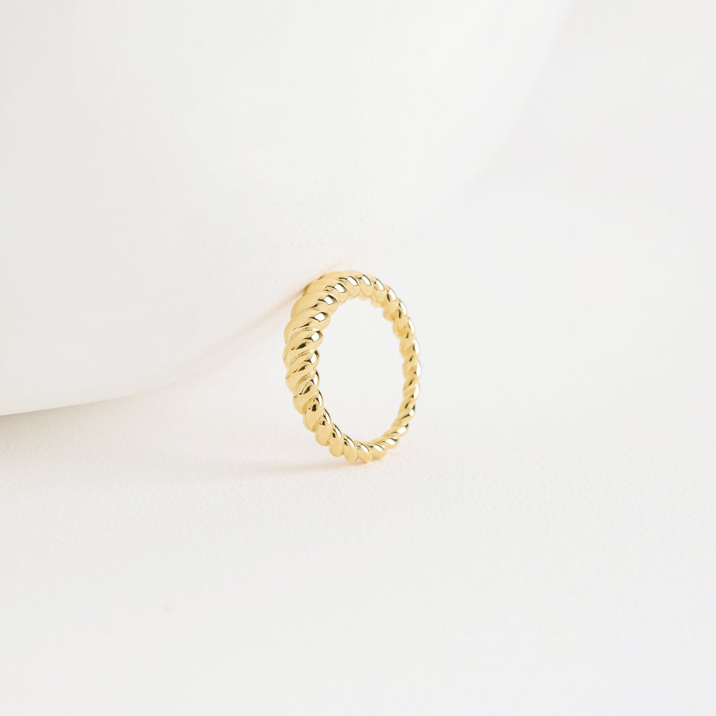 The Twisted Dome Ring stands upright on a white surface, its elegant gold curves highlighted against a minimal, clean background.