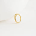 The Twisted Dome Ring stands upright on a white surface, its elegant gold curves highlighted against a minimal, clean background.