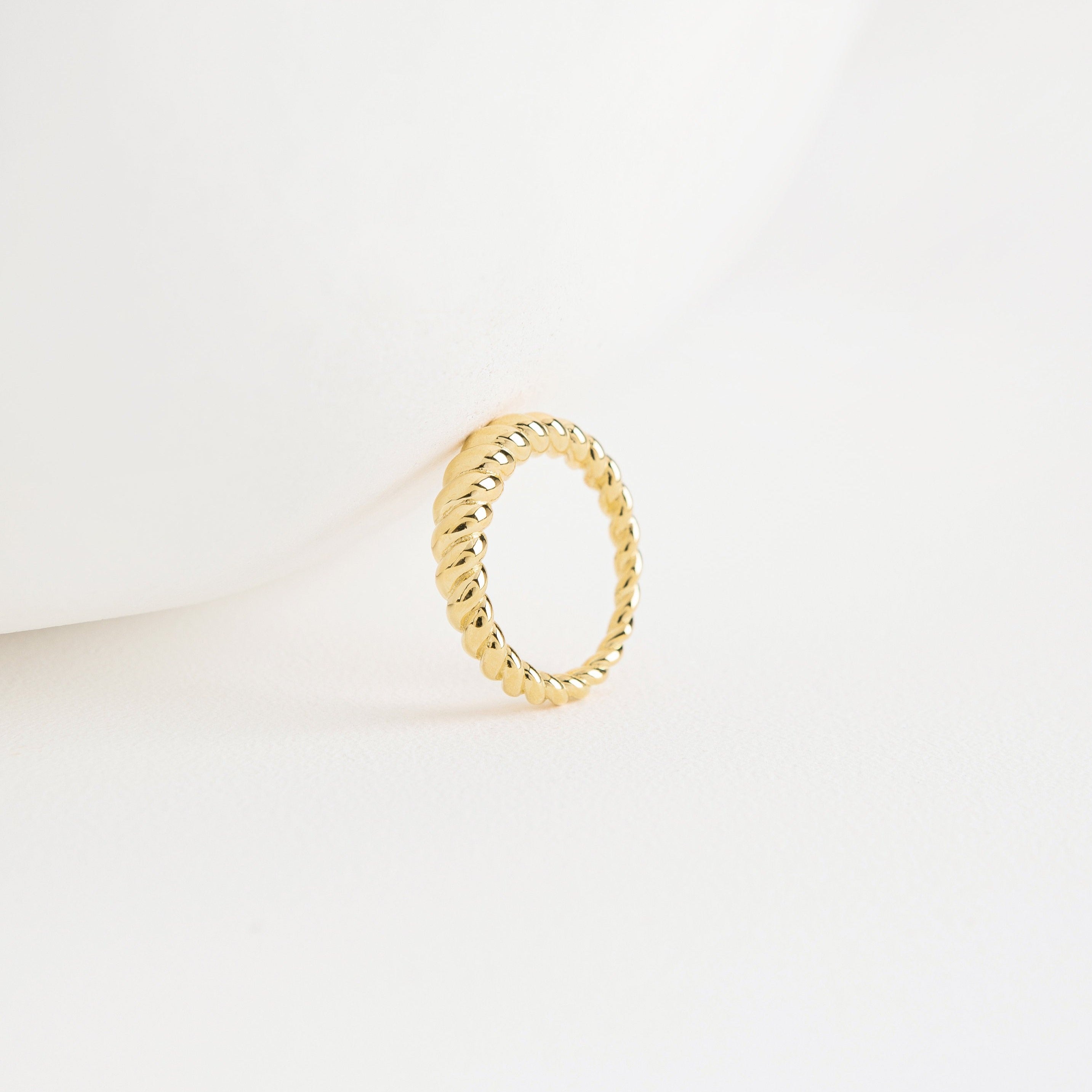 The Twisted Dome Ring stands upright on a white surface, its elegant gold curves highlighted against a minimal, clean background.