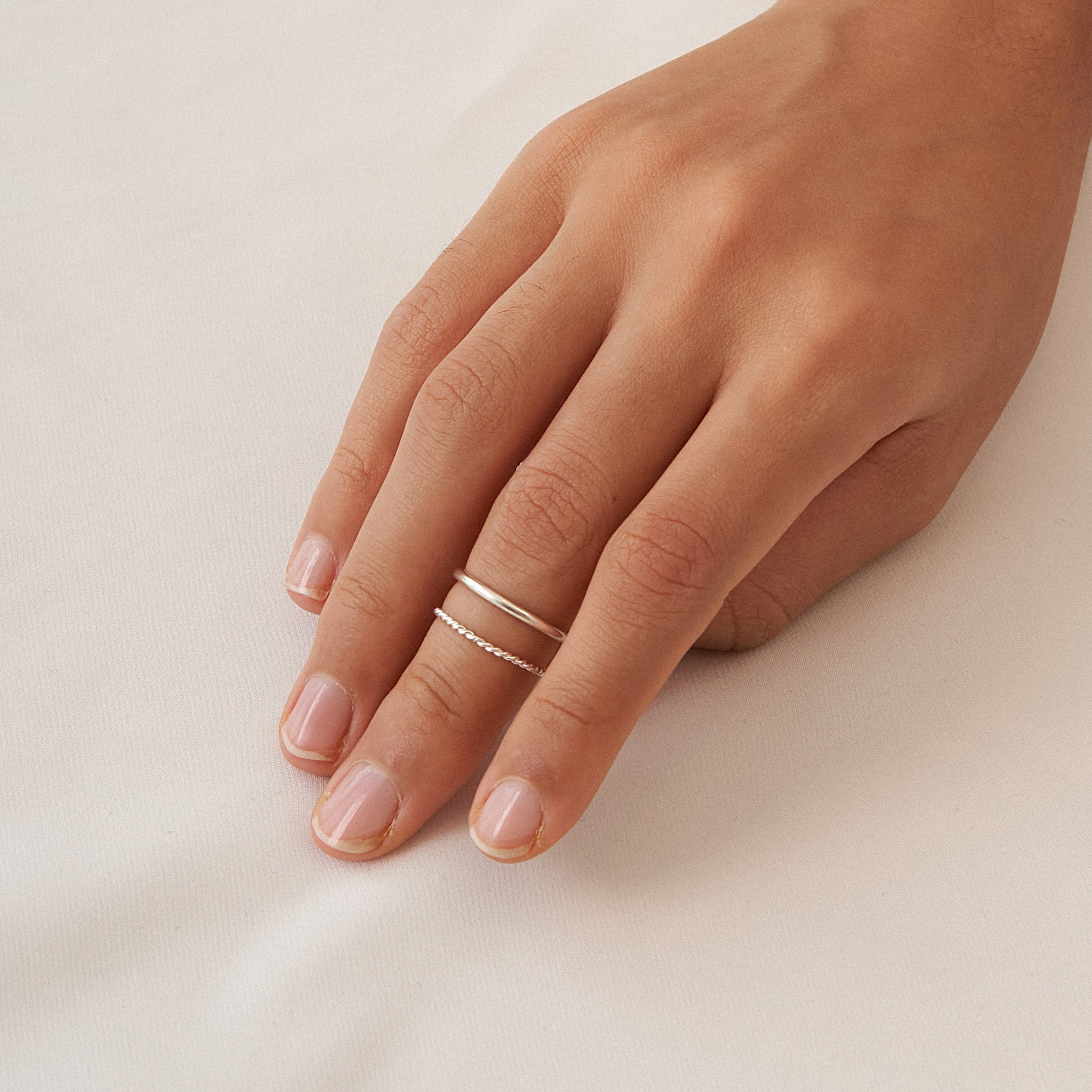 A hand adorned with the Minimalist Stacking Ring Set, featuring two gold stacking rings, rests gently on a white fabric surface.