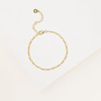 The Essential Bracelet Chains feature a delicate gold chain with an adjustable clasp and polished finish, showcased on a white textured surface.