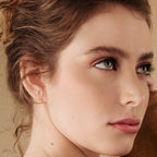 Close-up of a woman with light eyes, natural makeup, and minimal ear jewelry—gold Arc Studs featuring a small butterfly design.