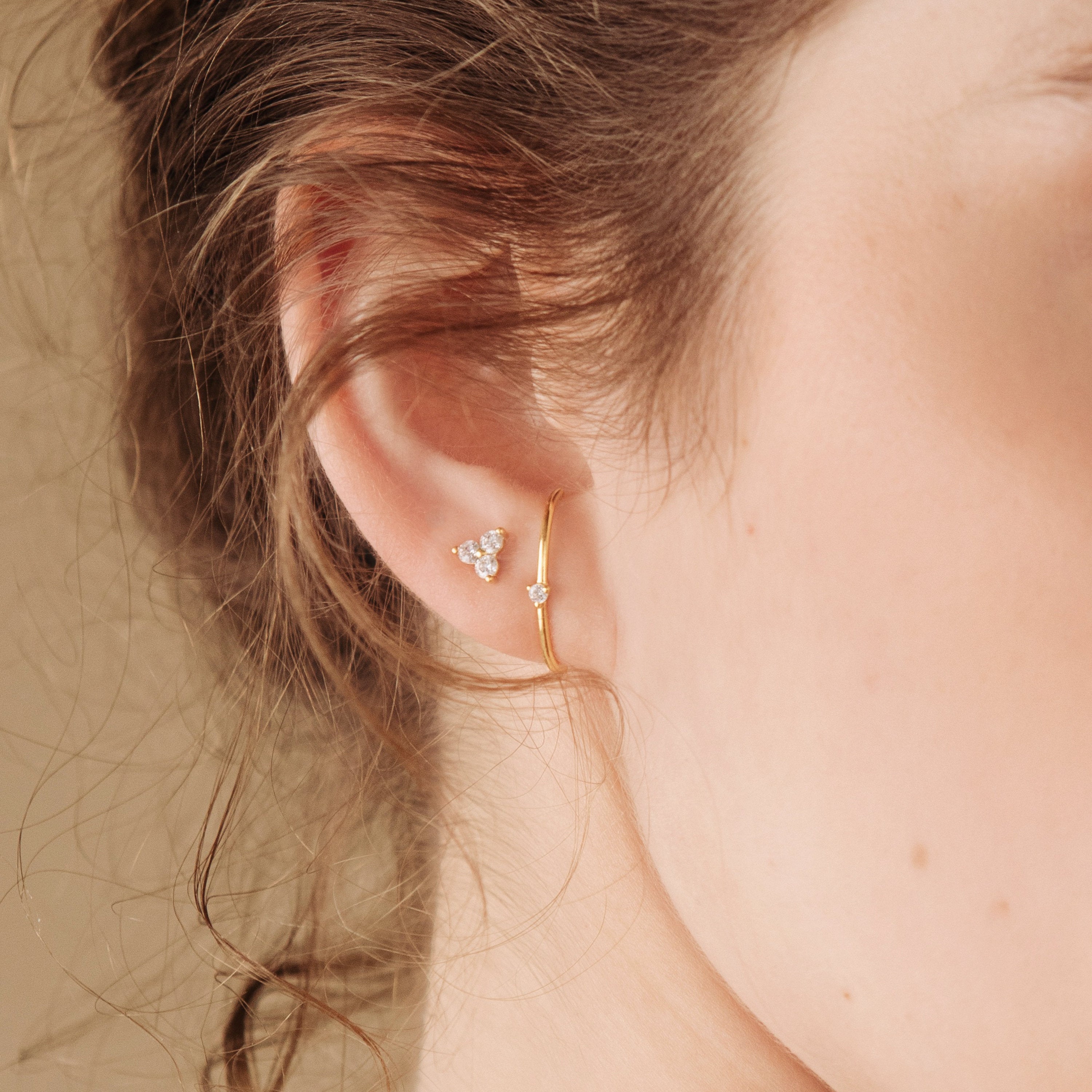 Close-up of a woman's ear wearing gold hoops and the Arc Studs—a delicate trio of gem-shaped stud earrings, perfect for fans of minimal arc jewelry.