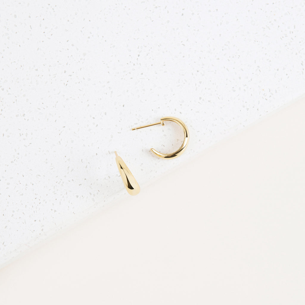 Two Dome Hoops lie elegantly on a white and cream textured background, offering a refined, minimalist take on chunky hoop earrings.