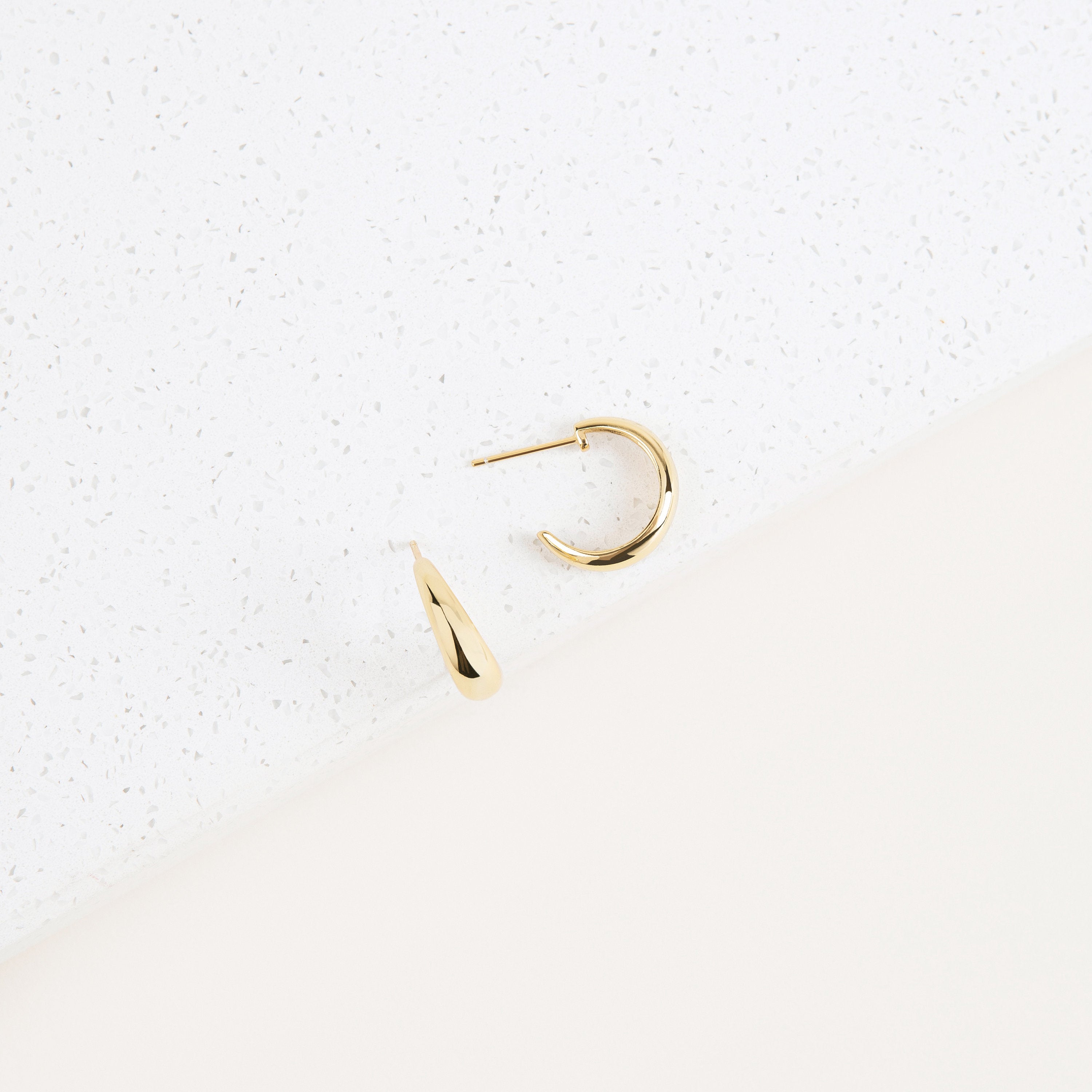 Two Dome Hoops lie elegantly on a white and cream textured background, offering a refined, minimalist take on chunky hoop earrings.
