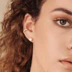 Close-up of a woman’s ear adorned with Zoe Pearl Studs—a contemporary pearl earring—paired with a gold cuff, framed by curly hair and subtle, neutral makeup.