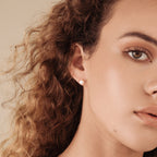 A close-up of a woman with curly hair wearing the Zoe Pearl Studs, highlighting the elegance and modern style of these feminine pearl earrings from the side.