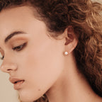 A woman with curly hair wears a Zoe Pearl Stud earring in a close-up side profile, highlighting contemporary jewelry style and timeless feminine elegance.