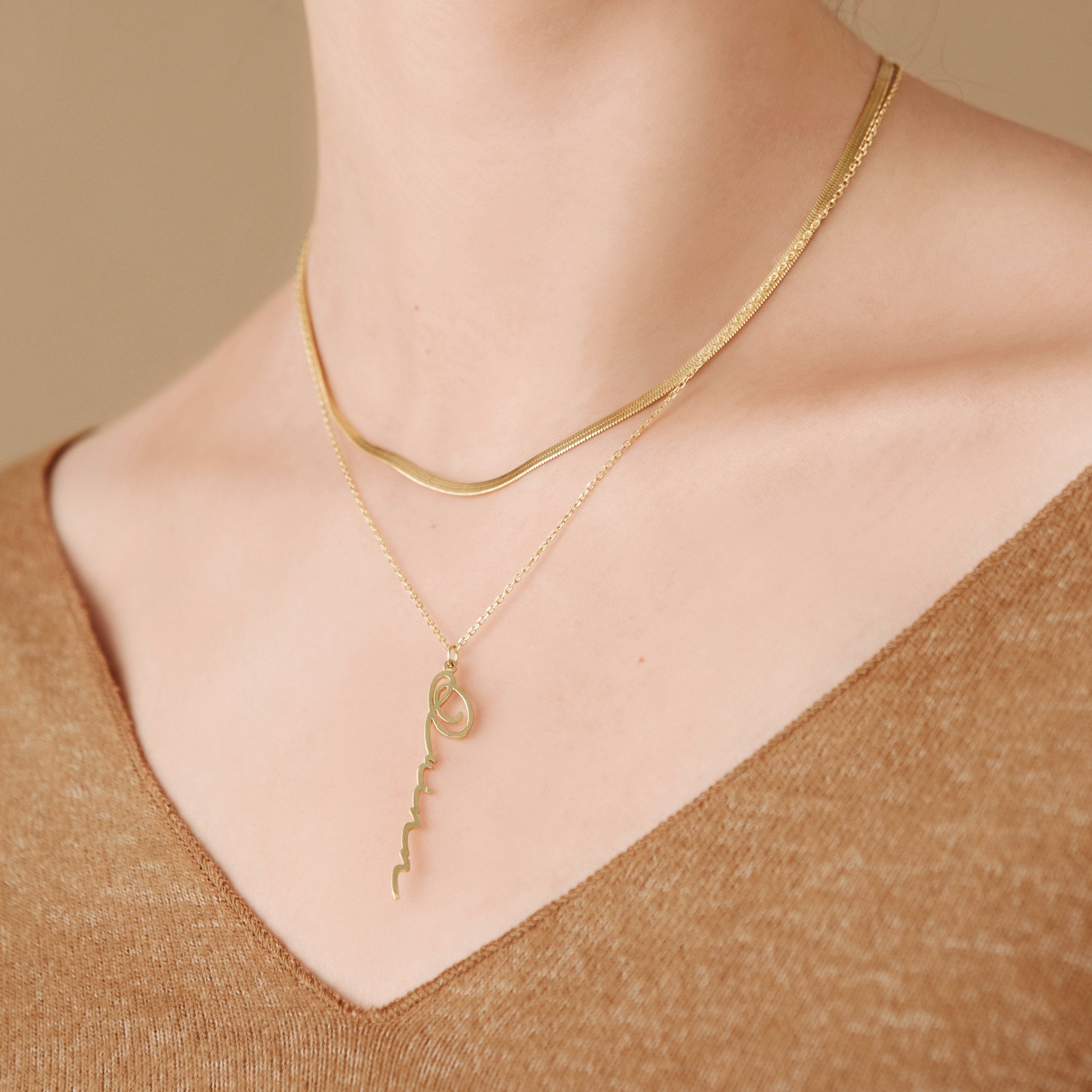 A model wearing the gold herringbone necklace paired with a personalized script pendant necklace