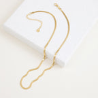 A close-up view of a gold herringbone necklace resting on a terrazzo display block.